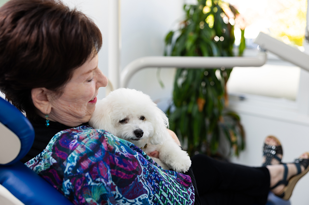 Comfort-Focused Dental Care with an Emotional Support Dog Patient holding an emotional support dog while relaxing in a dental chair at iCreate Smiles in Palo Alto